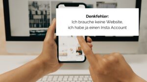 Eine Hand hält ein Smartphone und bedient es mit der anderen Hand, im Hintergrund ist eine Website auf einem Computer Bildschirm zu sehen.